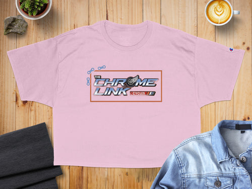 Pink cropped t-shirt with "The Chrome Link Cycles" logo on a wooden background.
